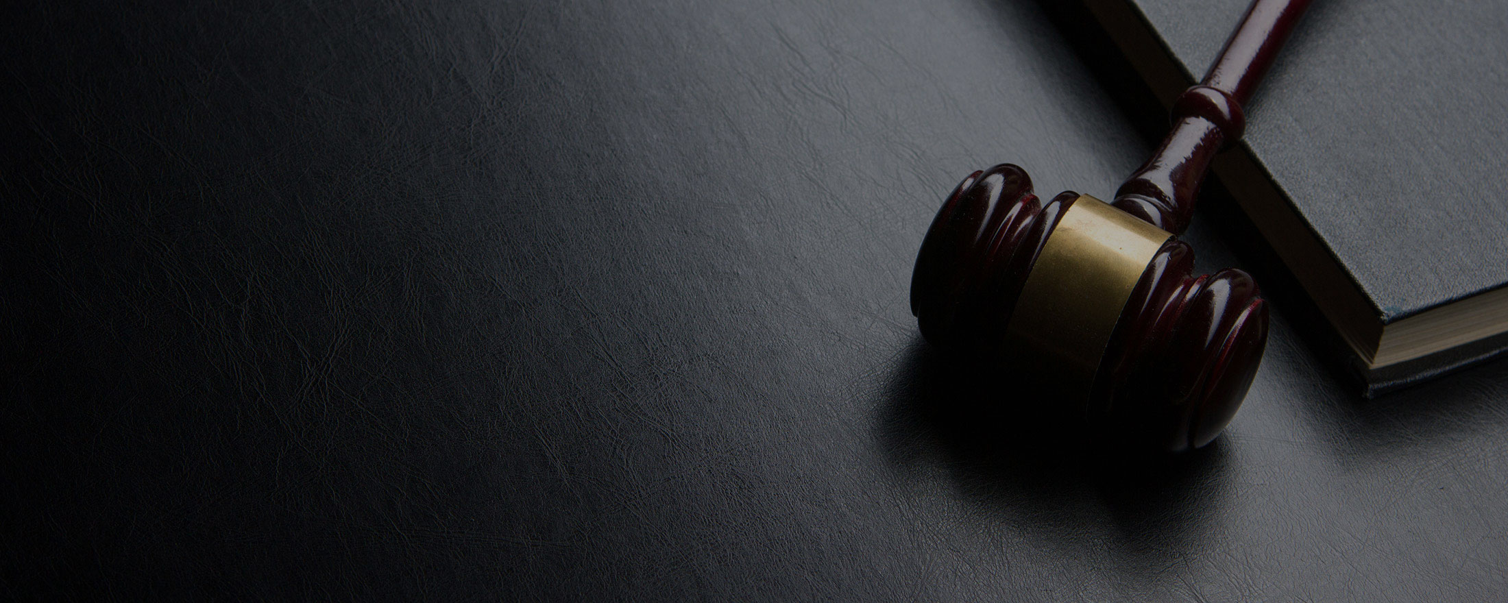 Law Better. Do Better. Wooden judge's gavel resting on a dark table beside a closed law book, conveying legal judgment imagery.