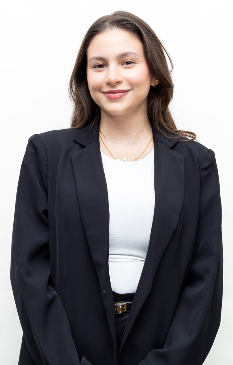 Professional headshot: young woman in a black blazer and white top, smiling at the camera against a plain white background.