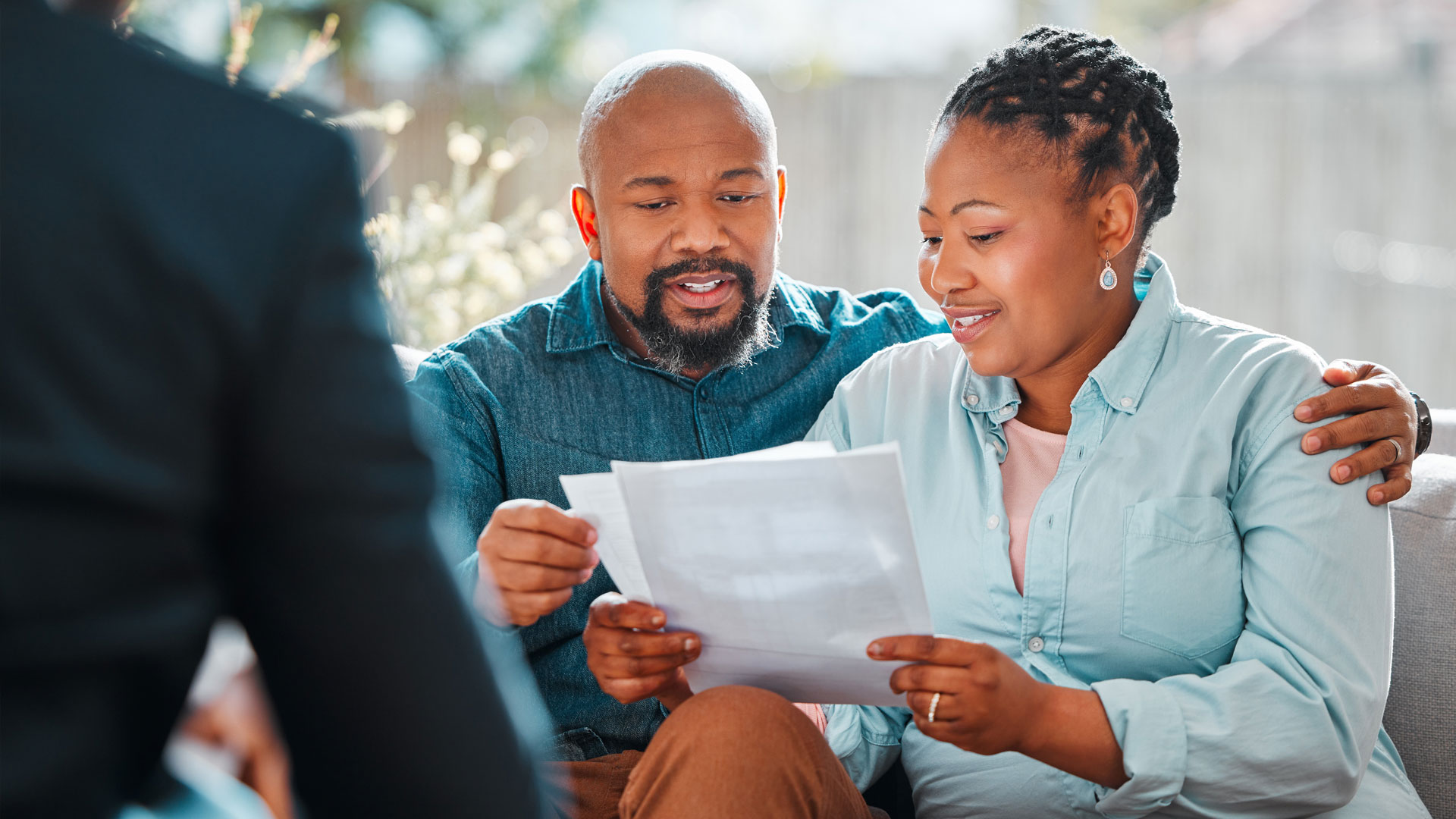 Areas of Practice: Estate Planning Areas of Practice: Estate Planning | A couple sits on a couch, smiling as they read papers together. The setting is bright and relaxed, suggesting a positive, supportive atmosphere.
